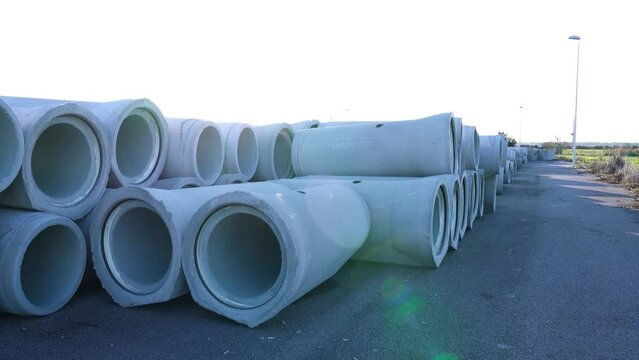 Motion past large pile of concrete pipes ready to install lying on asphalt ground at open construction site on sunny day