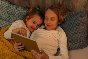 Sister cuddling in bed watching videos on tablet,it's bedtime and they don't want to go to sleep