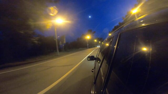 Black suv passing city highway at night. Auto riding through town streets in evening. Vehicle moving fast along motorway. Traffic on urban areas. Road trip or journey concept. Point of view