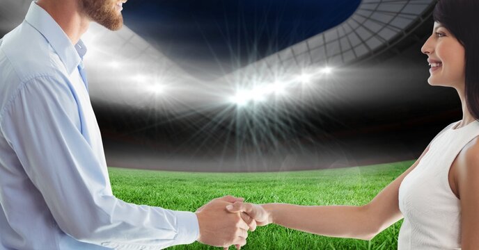 Composition of businessman and businesswoman shaking hands over sports stadium