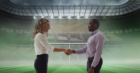 Composition of businessman and businesswoman shaking hands over sports stadium