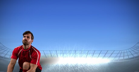 Composition of sportsman kneeling over sports stadium and blue sky