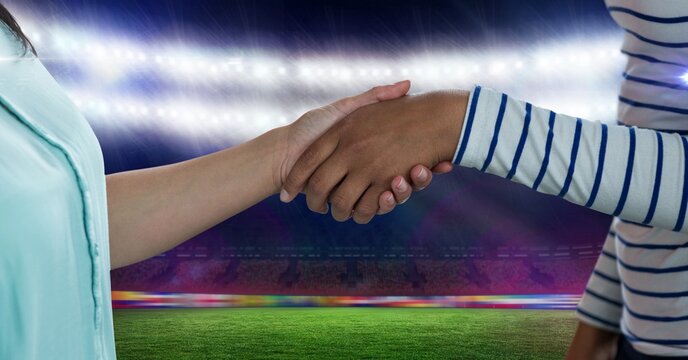 Composition of two businesswomen shaking hands over sports stadium