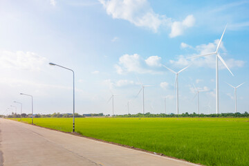 Concrete road in rural Thailand through green fields and wind turbine farm in background To produce clean, environmentally friendly and sustainable electricity