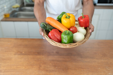 Healthy and strong Asian fit man wearing apron preparing vegetable baskets in kitchen at home before cooking online happily stay healthy and safe from disease.