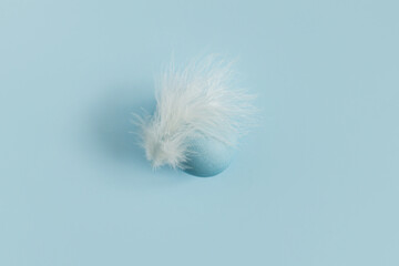 Stylish easter egg and feather on blue background flat lay. Minimal Easter still life. Modern...