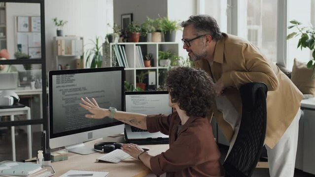 Two programmers discussing computer codes in team pointing at computer monitor in modern office