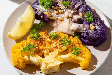 Close-up of vegetable colorful cauliflower steaks with herbs, spices and pine nuts on gray background. Vegan or vegetarian meal. Healthy plant based food.