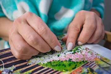 Close view of a woman hands embroidering a picture with beads. DIY. SDOF.