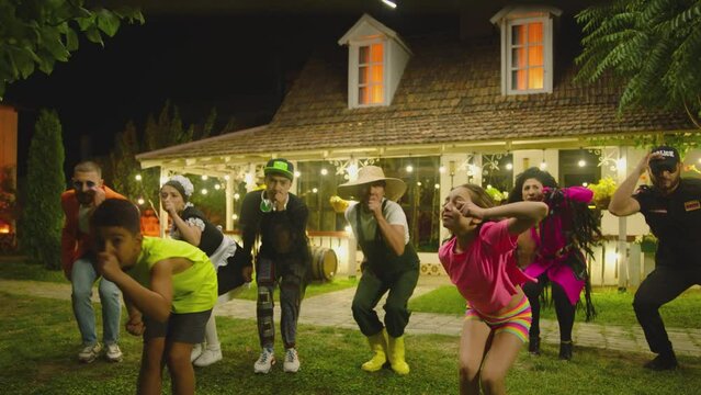 Group of funny , stylish  multi aged dancers dancing near village house at night . Kids dancing with house workers . Multi ethnic people having fun . Beautiful background with different lights .