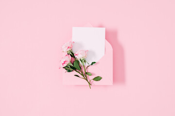 Top view on open pink envelope with paper card, bouquet of pink flowers rose on pastel pink table background. Birthday, Wedding, Mother's Day, Valentine's day, Women's Day. Flat lay, copy space