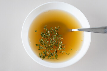 Bone broth with herbs in a white bowl with a spoon.