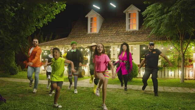 Group of funny , stylish  multi aged dancers dancing near village house at night . Kids dancing with house workers . Multi ethnic people having fun . Beautiful background with different lights .
