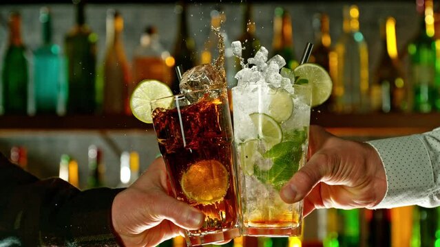 Super slow motion of cheering cocktail drinks in bar. Filmed on high speed cinema camera, 1000 fps. Bar with bottles on background.