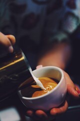 Close up barista hands making coffee latte art over dark background.