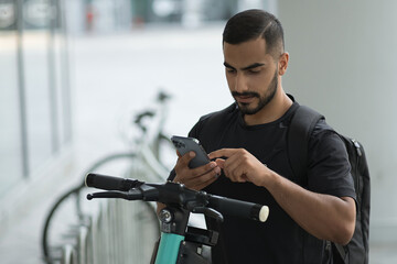 Serious man unlocking electric scooter with mobile phone while preparing ride