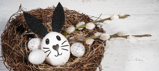 Happy Easter background banner holiday greeting card - Close-up of funny easter bunny, easter eggs and catkins in easter nest on white wooden table