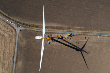 Wind turbine maintenance. A crane and some workers are hanged on the propeller to repair it. Wind eolian energy industry, aerial view.
