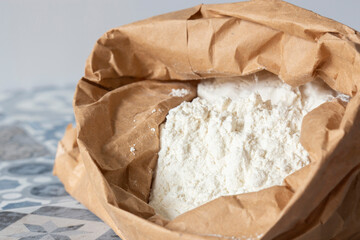 Plain white flour in a brown paper bag on blue tiled worktop. Eco friendly biodegradable recycle packaging