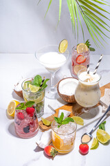 Summer cocktails drinks. Classic alcoholic long drink mocktail versions, various beverages, lemonades with berries, lime, orange, coconut, ice on white marble background 