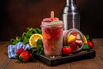 Frozen mocktail, popsicle punch with fruit and berry. Iced summer sangria with strawberry, orange, apple and fruit juice, with ingredients on wooden kitchen table background 
