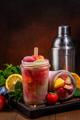 Frozen mocktail, popsicle punch with fruit and berry. Iced summer sangria with strawberry, orange, apple and fruit juice, with ingredients on wooden kitchen table background 
