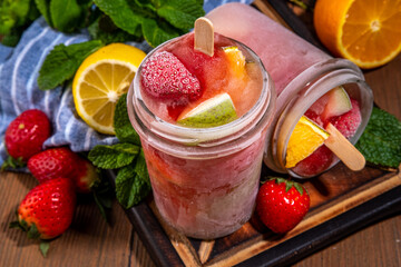 Frozen mocktail, popsicle punch with fruit and berry. Iced summer sangria with strawberry, orange, apple and fruit juice, with ingredients on wooden kitchen table background 
