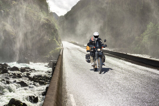 Motorbike driving fast on wet canyon valley road and bridge across river. Motobiker journey in Norway.