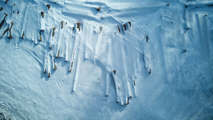 Logs under snow on meadow in forest. Pile of firewood in winter. Many chopped logs. Pile of firewood covered in snow. Firewood under the snow. Wood fuel. Top down aerial view.