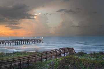 Sunrise over the ocean with lit pier and green covered dunes