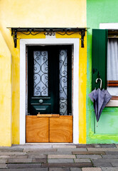 Brightly Coloured Yellow & Green Houses Of Burano With An Umbrella Hung Up Outside