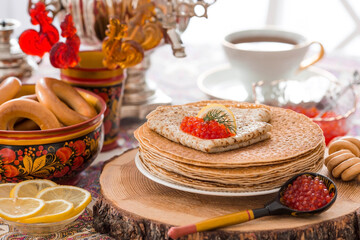 Russian traditions. Russian holiday Maslenitsa. Still life with a cup of tea, a stack of pancakes, red caviar, lemon, bagels, a lollipop cockerel, wooden spoons (khokhloma) and samovars.