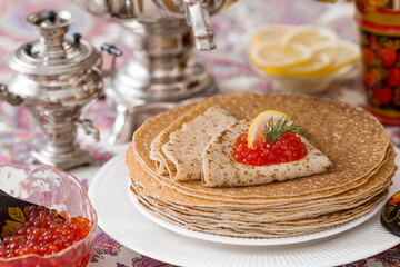 Russian traditions. Russian holiday Maslenitsa. Still life with a cup of tea, a stack of pancakes, red caviar, lemon, bagels, a lollipop cockerel, wooden spoons (khokhloma) and samovars.