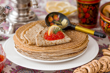 Russian traditions. Russian holiday Maslenitsa. Still life with a cup of tea, a stack of pancakes, red caviar, lemon, bagels, a lollipop cockerel, wooden spoons (khokhloma) and samovars.