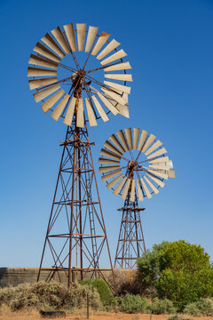 Looking up at wo large windmills against a blue cloudless sky