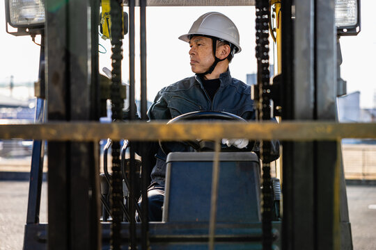 Middle-aged Asian male worker with forklift on factory grounds.