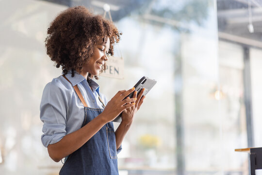 Successful African Woman In Apron Standing Coffee Shop Door. Happy Small Business Owner Holding Tablet And Working. Smiling Portrait Of SME Entrepreneur Seller Business Standing With Copy Space.