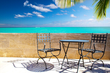 an empty street bar, cafe or restaurant with an old wrought iron table and chairs standing near a colonial stone wall overlooking a seascape with palm trees. Tropics, summer, sunny day