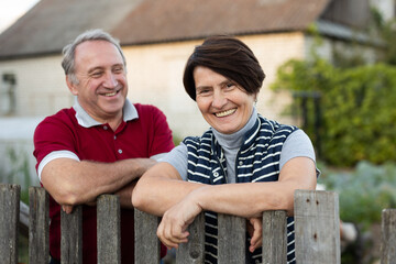 Elderly couple standing together near wooden fence in garden