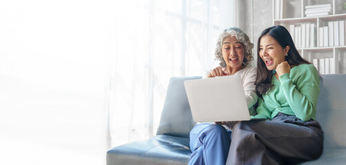 60s asian mother elderly sitting on sofa with young asia female daughter together in living room. watch movies series online or shopping, using laptop computer