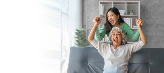 60s asian mother elderly sitting on sofa with young asia female daughter together in living room. happy surprised