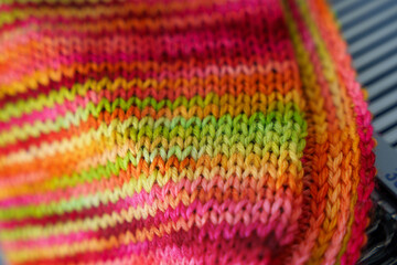An openwork of colorful woolen scarf. Merino scarf on flat bed knitting machine. Simple Stockinette stitch is one of the most basic knitting patterns. Knit fabric used in scarves.