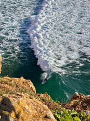 take of of a surfer in a green wave under a cliff