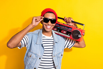 Photo of cheerful carefree man arm touch sunglass carry boombox toothy smile isolated on yellow color background