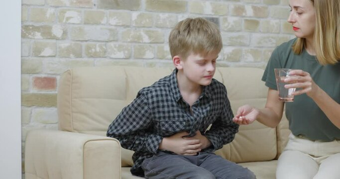 Boy has a stomach ache. Mom gives boy a pill with water.