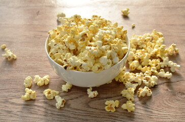 salty popcorn spreading  from bowl on wooden table 