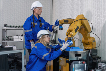 Female senior robotic engineer in modern factory teach new comer operate and maintenance robot arm