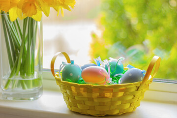 yellow basket with Easter colorful eggs on window sill with flowers.