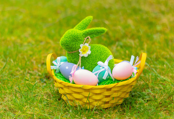 green grass rabbit in basket with colorful eggs on the meadow. Easter symbol, decor, bunny figure