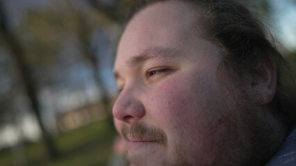 Obraz premium One thoughtful chubby young man relaxed outdoors close up face. Pensive millennial guy smiling in contemplation in nature